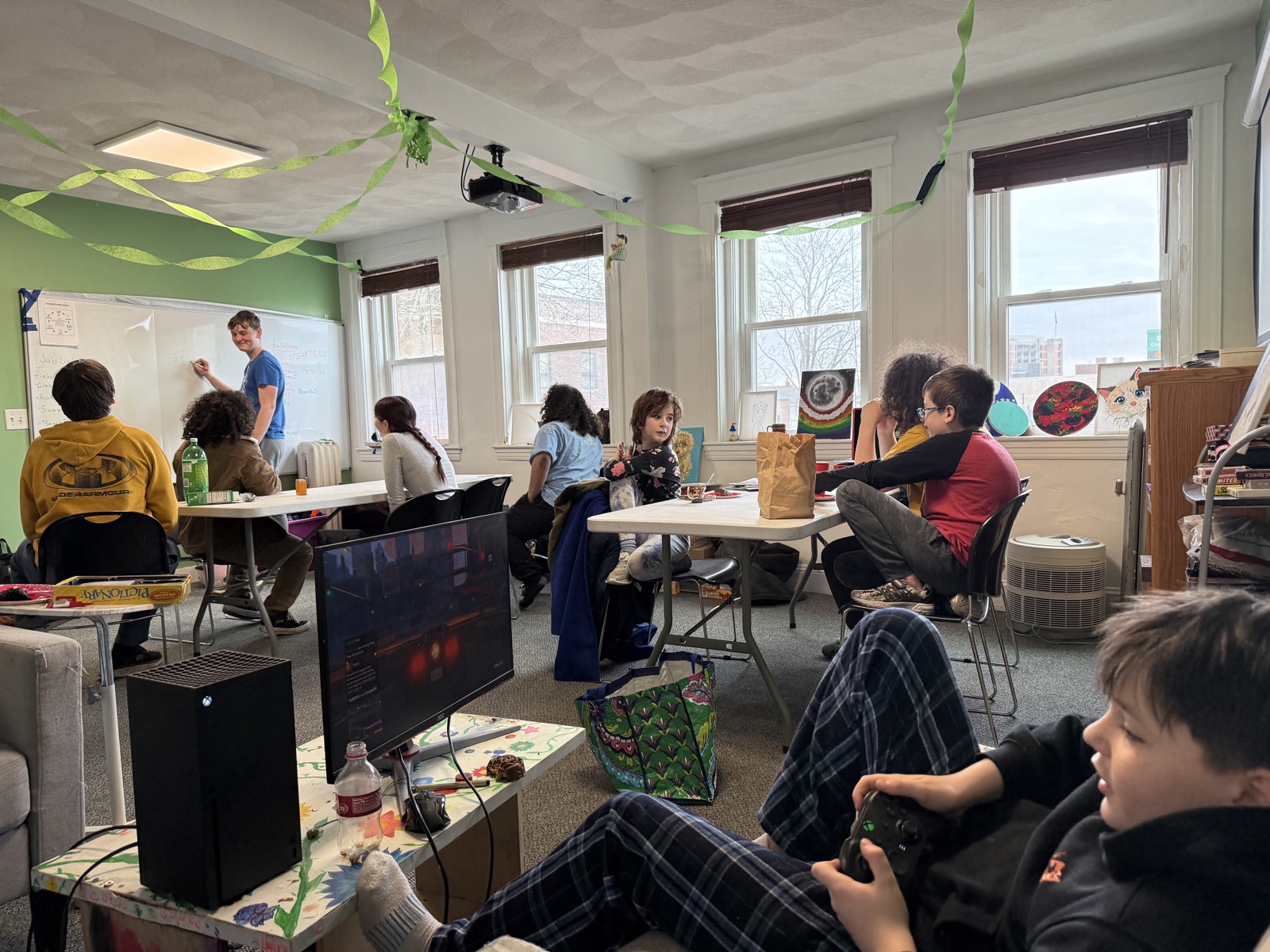A busy Pathfinder room, with a student teaching at the whiteboard while others work at tables